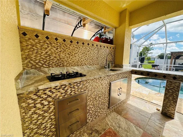 View of patio with glass enclosure, sink, and an outdoor kitchen