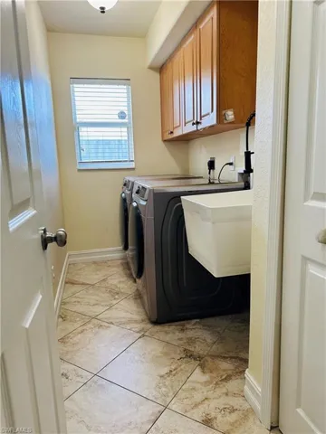 Washroom featuring sink, washing machine and dryer, light tile patterned floors, and cabinets