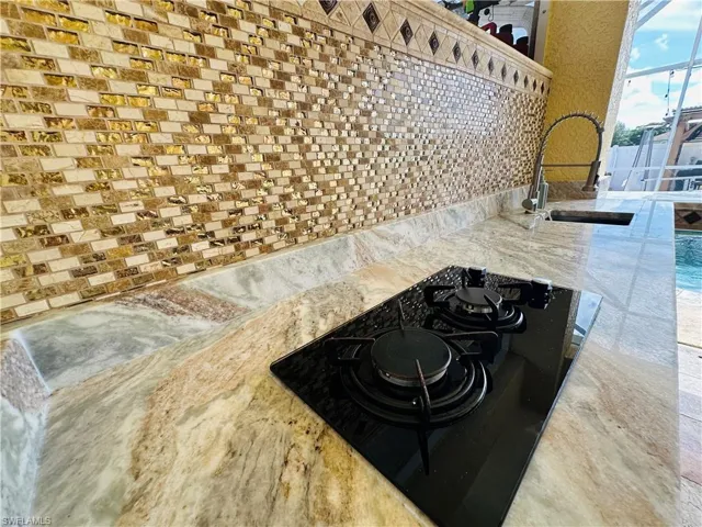 Interior details featuring stovetop, sink, light stone counters, and backsplash