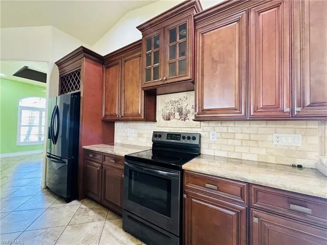 Kitchen with light tile patterned floors, vaulted ceiling, decorative backsplash, and black appliances