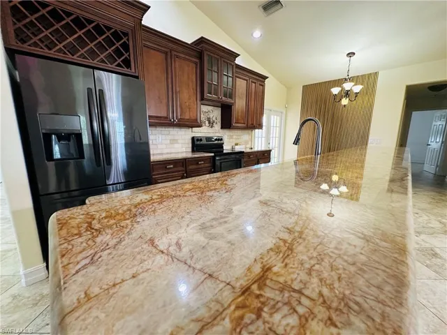 Kitchen featuring backsplash, range with electric cooktop, light stone countertops, stainless steel fridge with ice dispenser, and an inviting chandelier