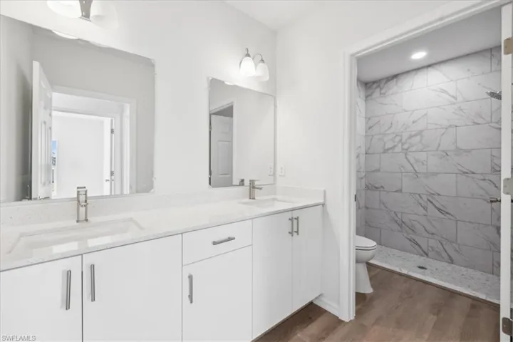 Bathroom featuring tiled shower, hardwood / wood-style floors, vanity, and toilet