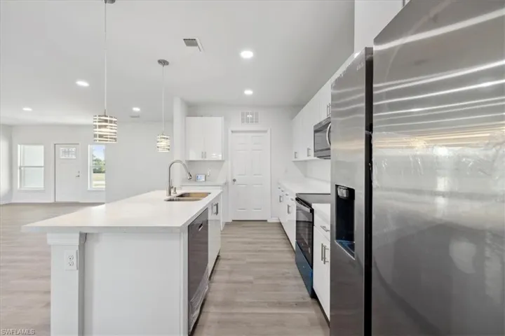 Kitchen featuring sink, hanging light fixtures, light hardwood / wood-style flooring, appliances with stainless steel finishes, and white cabinetry