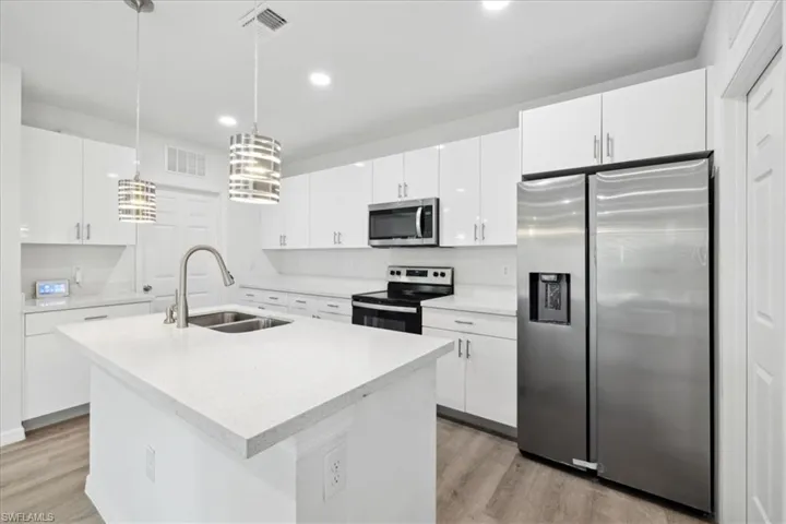 Kitchen featuring white cabinetry, sink, hanging light fixtures, and appliances with stainless steel finishes
