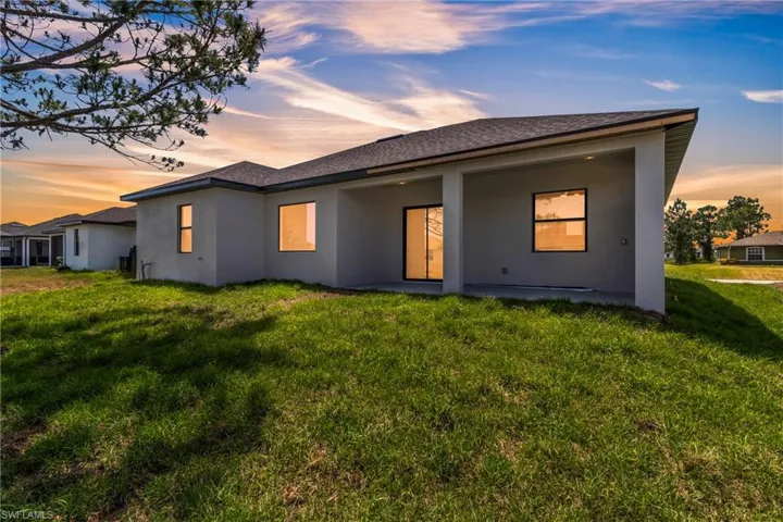 Back of property with stucco siding, a lawn, and a shingled roof