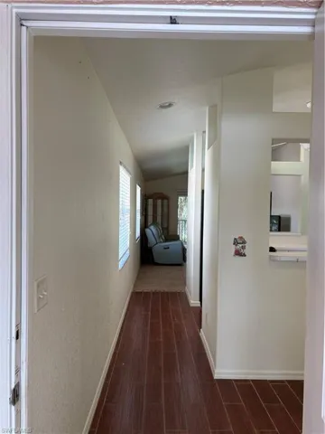 Corridor with dark wood-style floors, a textured wall, and vaulted ceiling