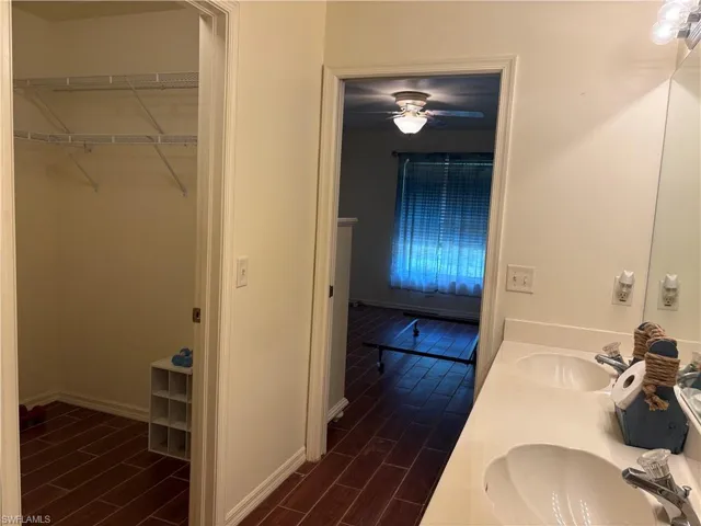 Bathroom featuring wood tiled floors, double vanity, a ceiling fan, and a spacious closet