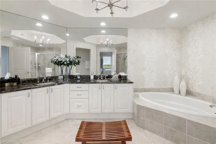Bathroom featuring a raised ceiling, double vanity, a shower stall, wallpapered walls, and a bath