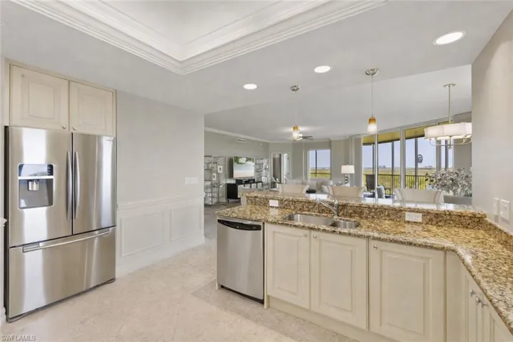 Kitchen featuring cream cabinets, appliances with stainless steel finishes, a decorative wall, pendant lighting, and light stone counters