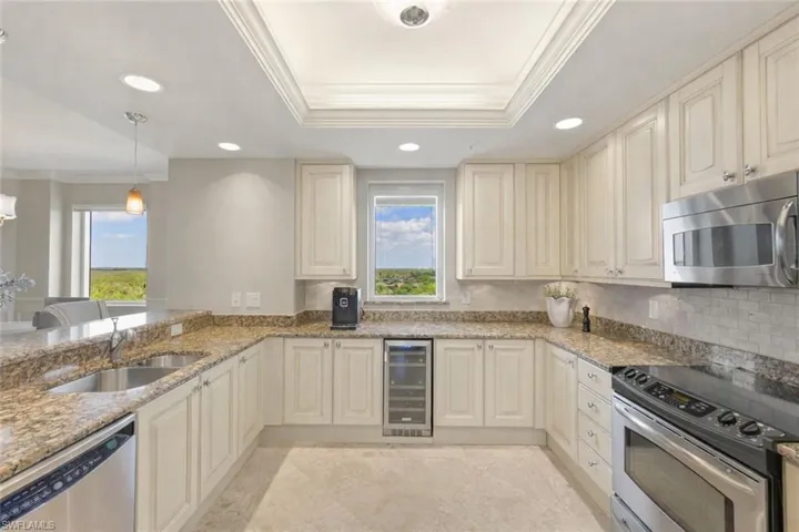 Kitchen with ornamental molding, appliances with stainless steel finishes, light stone counters, cream cabinetry, and hanging light fixtures