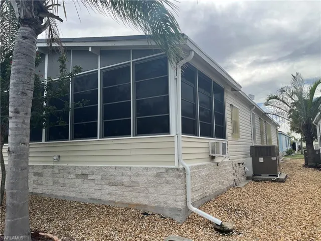 View of property exterior with a sunroom, central AC unit, and an AC wall unit