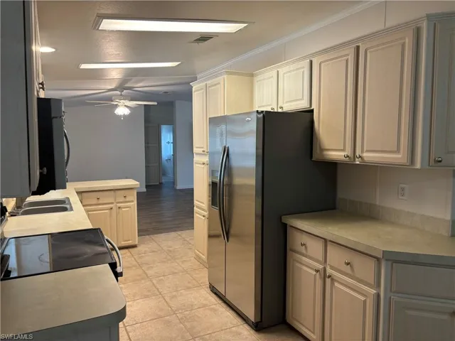 Kitchen with ornamental molding, stainless steel refrigerator with ice dispenser, sink, ceiling fan, and light tile floors