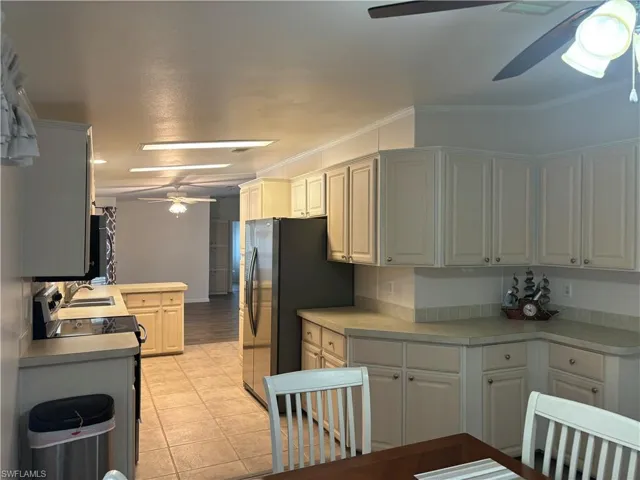 Kitchen with ceiling fan, light tile flooring, sink, stainless steel refrigerator, and ornamental molding