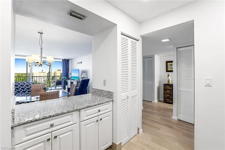Kitchen featuring light hardwood / wood-style flooring, pendant lighting, an inviting chandelier, light stone counters, and white cabinetry