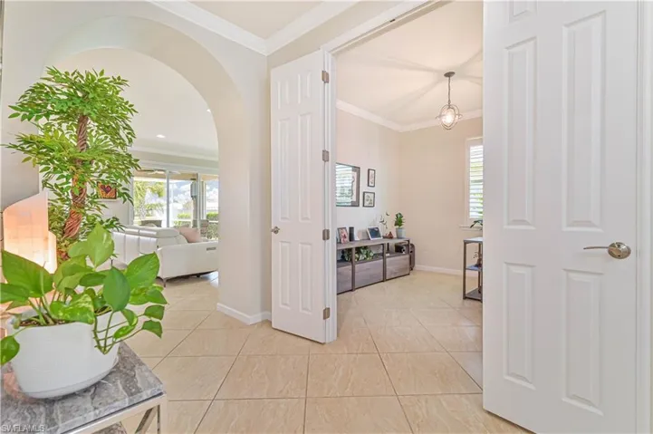Hall with arched walkways, plenty of natural light, crown molding, and light tile patterned flooring