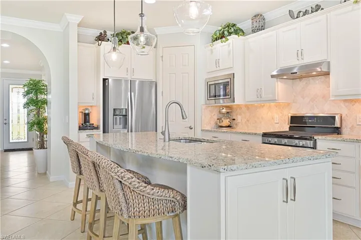 Kitchen featuring stainless steel appliances, under cabinet range hood, light tile patterned floors, crown molding, and an island with sink