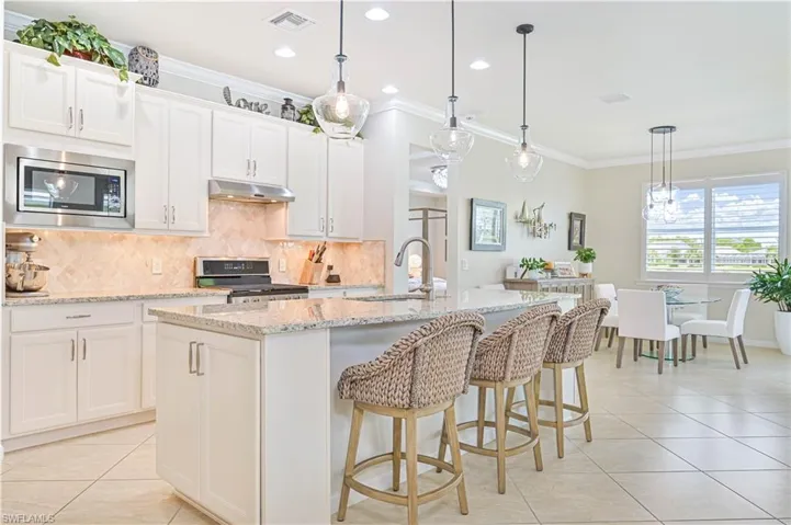 Kitchen with stainless steel microwave, range with electric stovetop, under cabinet range hood, light tile patterned floors, and backsplash