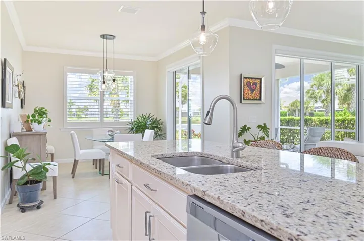 Kitchen with light tile patterned floors, light stone countertops, pendant lighting, white cabinetry, and crown molding
