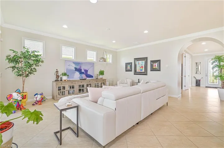 Living room featuring light tile patterned floors, arched walkways, ornamental molding, and recessed lighting