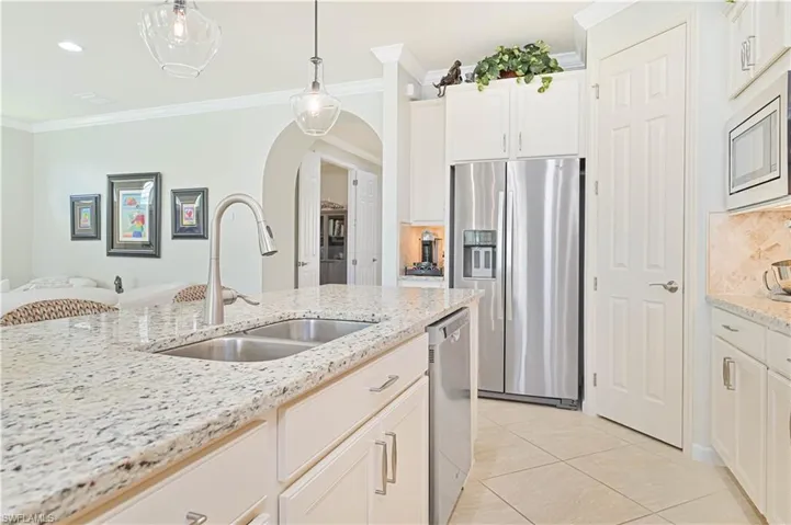 Kitchen featuring stainless steel appliances, crown molding, arched walkways, pendant lighting, and light tile patterned flooring