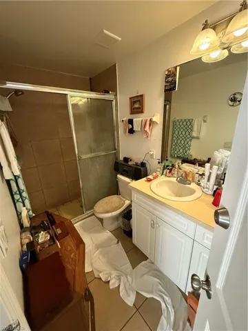 Bathroom featuring toilet, vanity, tile patterned floors, and a shower with door