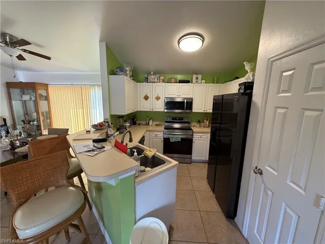 Kitchen with ceiling fan, light tile patterned flooring, kitchen peninsula, white cabinets, and appliances with stainless steel finishes