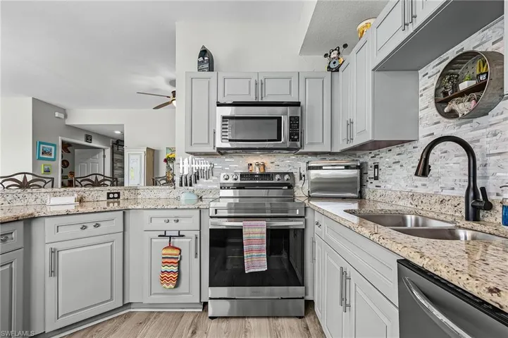 Kitchen featuring stainless steel appliances, light stone countertops, gray cabinets, a ceiling fan, and light vinyl finished floors