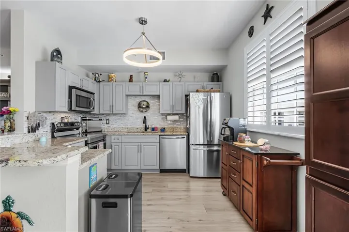 Kitchen featuring stainless steel appliances, decorative backsplash, pendant lighting, light vinyl floors, and gray cabinets
