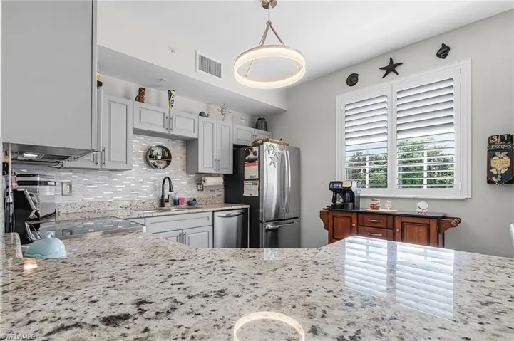Kitchen with light stone countertops, backsplash, stainless steel appliances, and hanging light fixtures