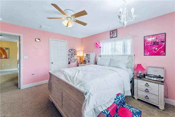 Carpeted bedroom featuring ceiling fan with notable chandelier