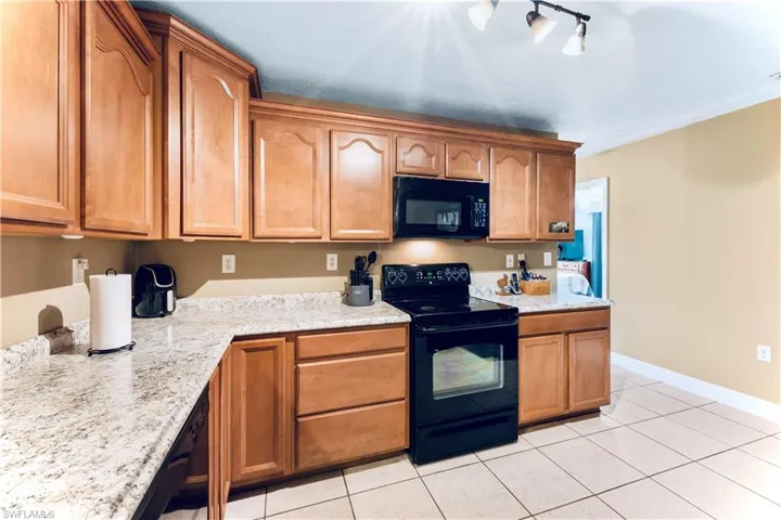 Kitchen featuring light stone counters, black appliances, track lighting, and light tile floors