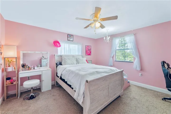 Bedroom with ceiling fan with notable chandelier and light colored carpet