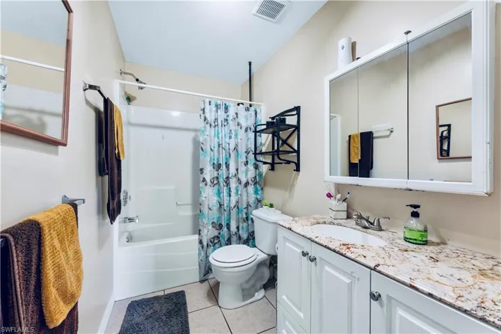 Full bathroom featuring shower / bath combo with shower curtain, vanity, toilet, and tile floors