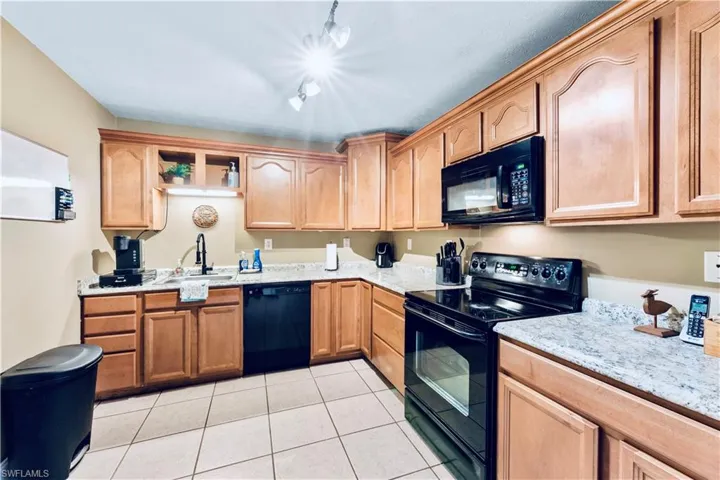 Kitchen with light stone countertops, sink, black appliances, and light tile floors