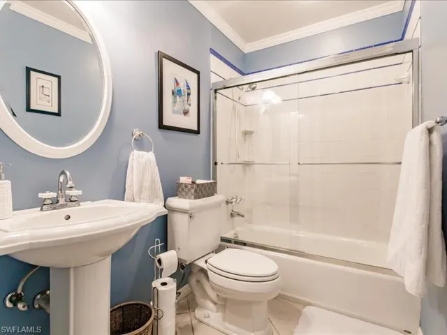 Bathroom with tile floors, ornamental molding, toilet, and bath / shower combo with glass door