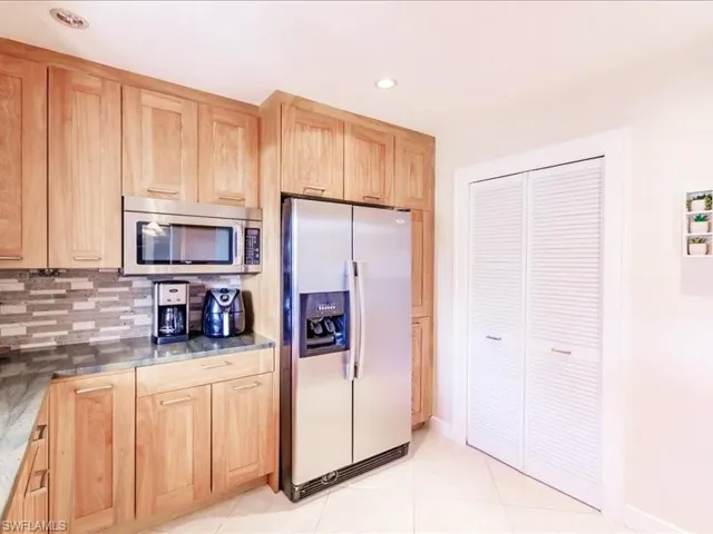 Kitchen featuring dark stone countertops, stainless steel appliances, backsplash, light tile floors, and light brown cabinets