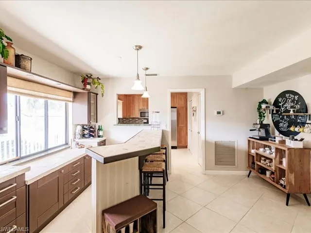 Kitchen with a breakfast bar, appliances with stainless steel finishes, decorative light fixtures, and light tile floors