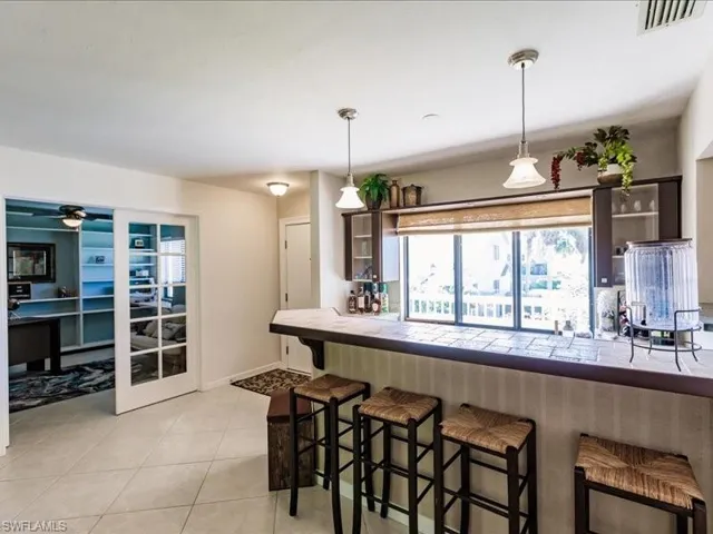 Kitchen with a breakfast bar area, tile countertops, decorative light fixtures, ceiling fan, and light tile floors