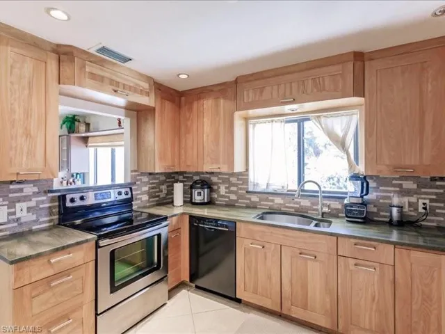 Kitchen with electric range, sink, black dishwasher, and backsplash
