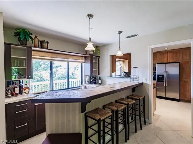 Kitchen with light tile floors, hanging light fixtures, stainless steel fridge with ice dispenser, and a breakfast bar