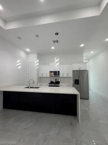 Spacious kitchen featuring a large island with a sink, white cabinetry, stainless steel appliances, and large format tile flooring