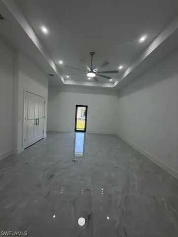 Spacious room featuring large format grey marble-effect tile flooring, a tray ceiling with recessed lighting, and a ceiling fan