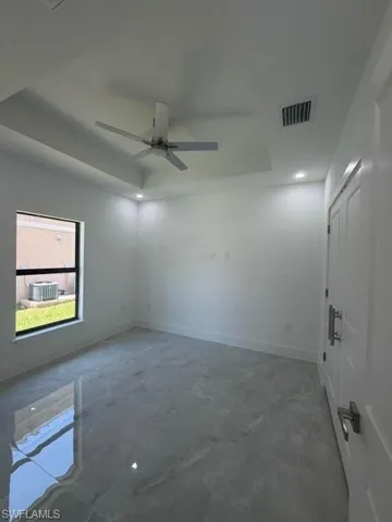 Spacious room featuring large format marble-look tile flooring, a tray ceiling with recessed lighting, and a modern ceiling fan