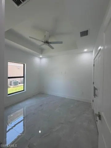 Spacious room featuring tray ceilings, recessed lighting, a ceiling fan, and large format polished tile flooring