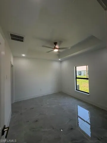 Spacious interior room featuring polished stone-look tile flooring, white walls, and a tray ceiling with recessed lighting