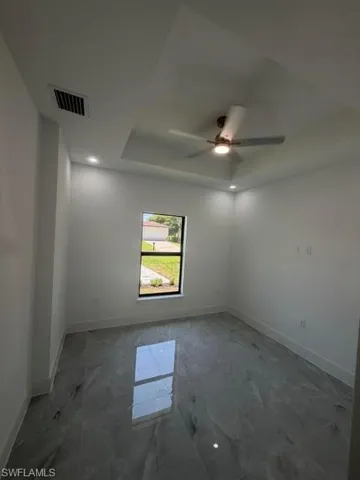 Spacious room featuring large format tile flooring, a tray ceiling, recessed lighting, and a ceiling fan with integrated lighting