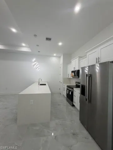 Kitchen featuring an expansive center island with an undermount sink, white shaker cabinetry, stainless steel appliances, and large format tile flooring
