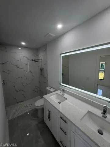 Contemporary bathroom featuring a double vanity with stone countertops, a large illuminated mirror, a tiled walk-in shower with a niche, and dark large-format floor tiles