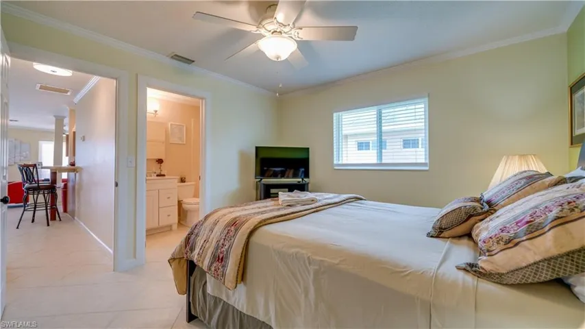 Tiled bedroom with crown molding, connected bathroom, and ceiling fan