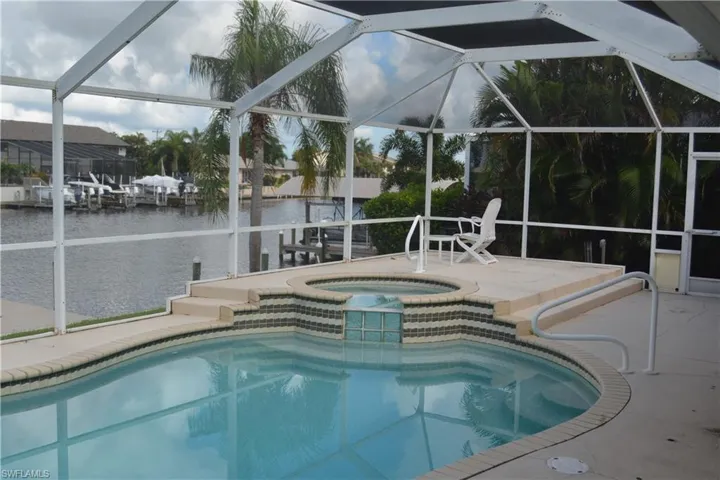 View of pool featuring a water view, a patio, a lanai, and an in ground hot tub